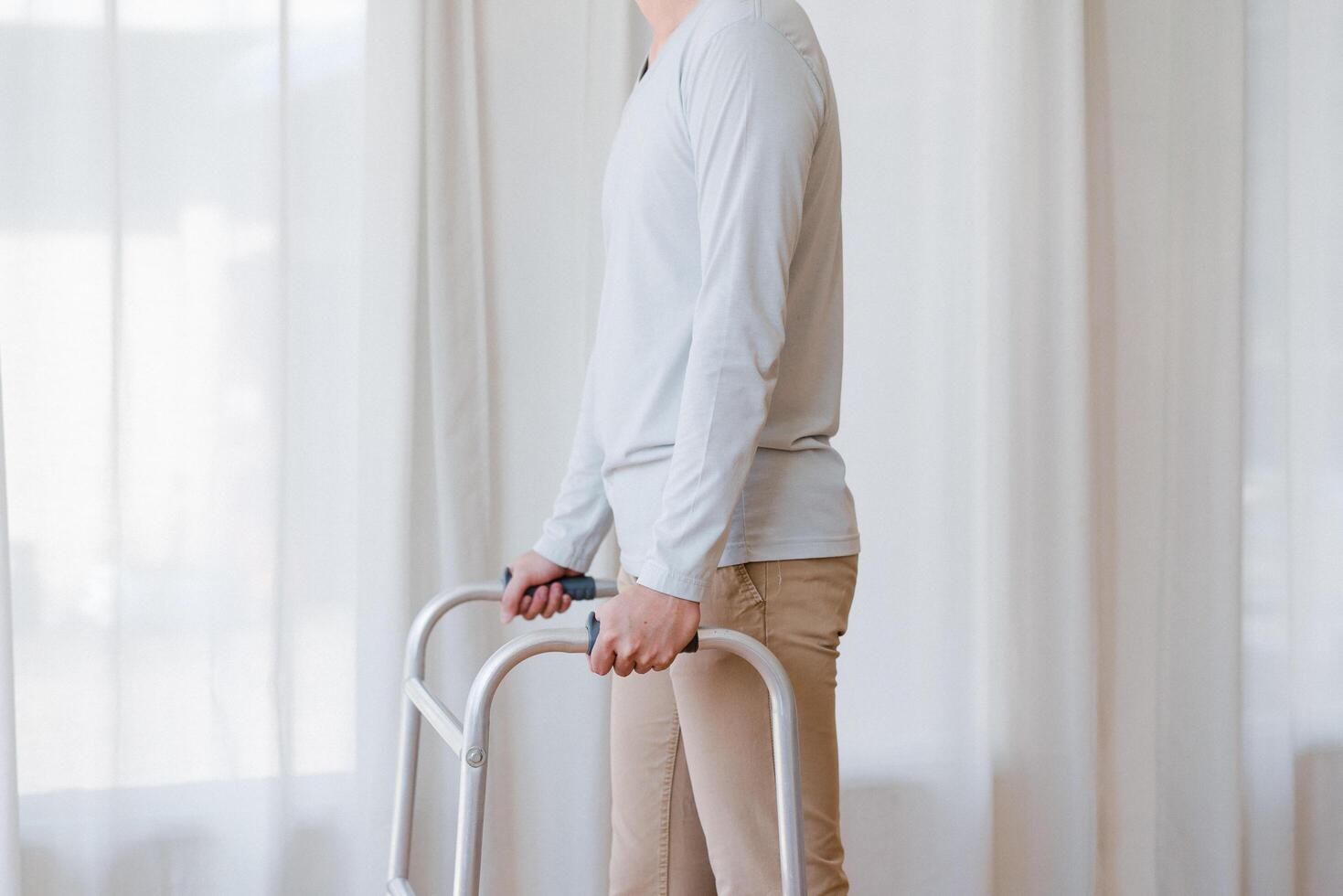 tondu vue de personnes âgées homme en marchant avec Cadre à maison, fermer. Jeune Masculin asiatique en utilisant médical équipement à bouge toi autour le sien maison. désactivée plus âgée la personne dans avoir besoin de professionnel Aidez-moi photo