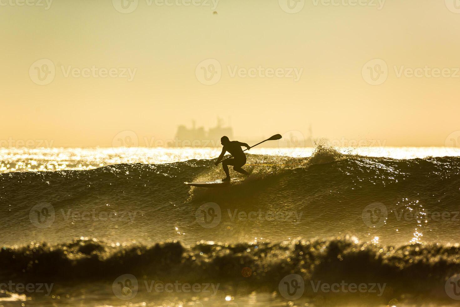 un non identifié surfeur monte une gros vague avec mousse à le coucher du soleil photo
