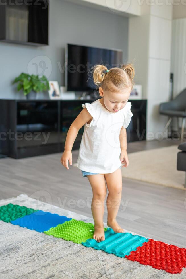 peu fille des promenades sur une massage tapis. bambin bébé pied massage tapis. des exercices pour jambes orthopédique massage tapis. photo