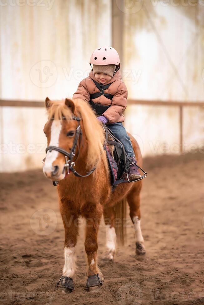 peu enfant équitation leçon. trois ans fille monte une poney et Est-ce que des exercices photo