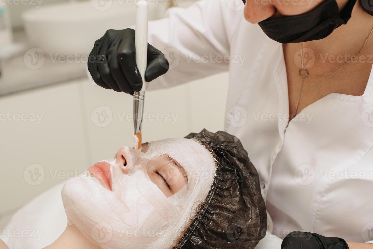 fermer de femelle professionnel cosmétologues mains appliquant masque à les patients visage pour faciale peau se soucier. photo