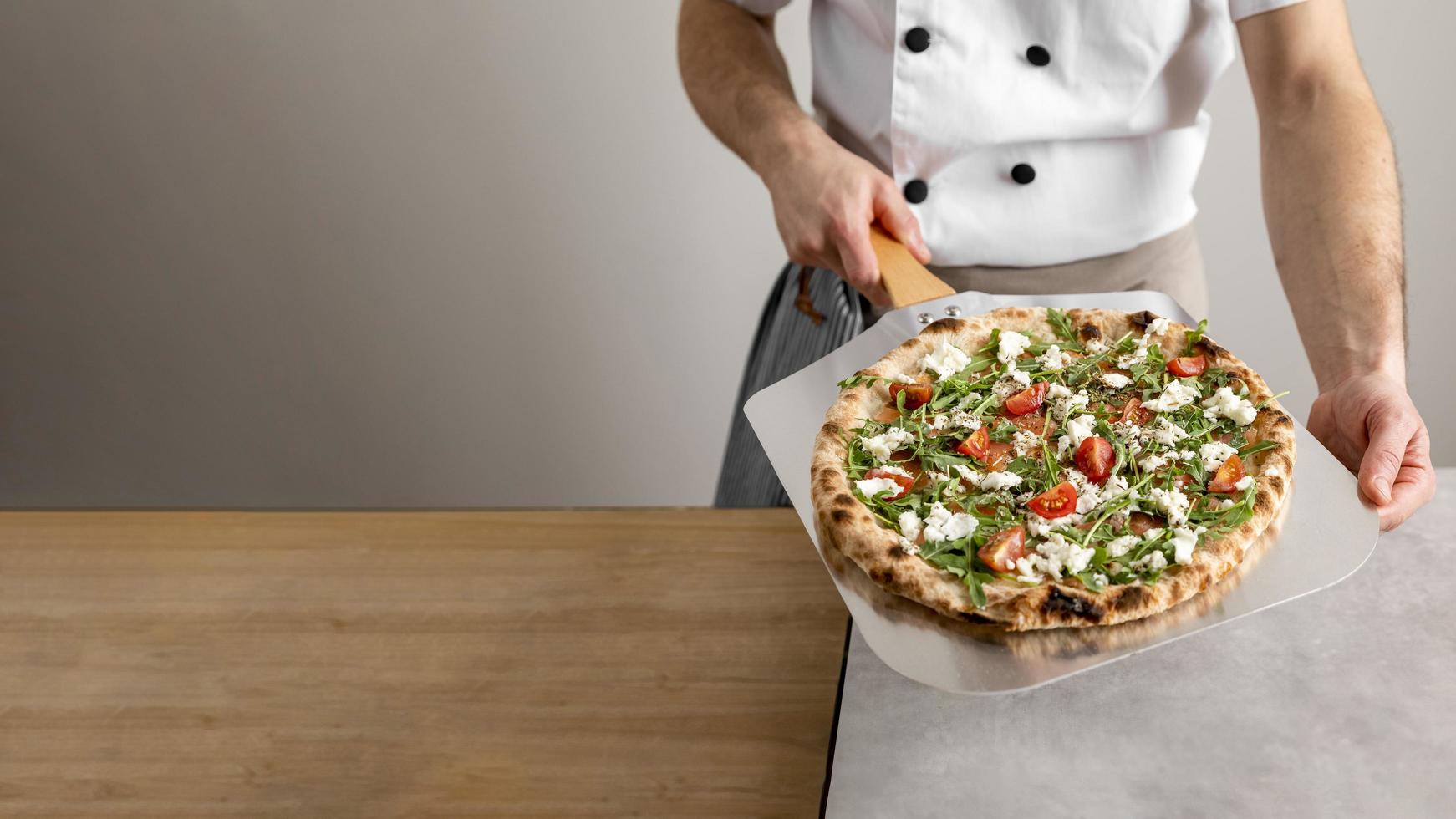 chef à angle élevé tenant un outil de pelage avec pizza. beau concept de photo de haute qualité