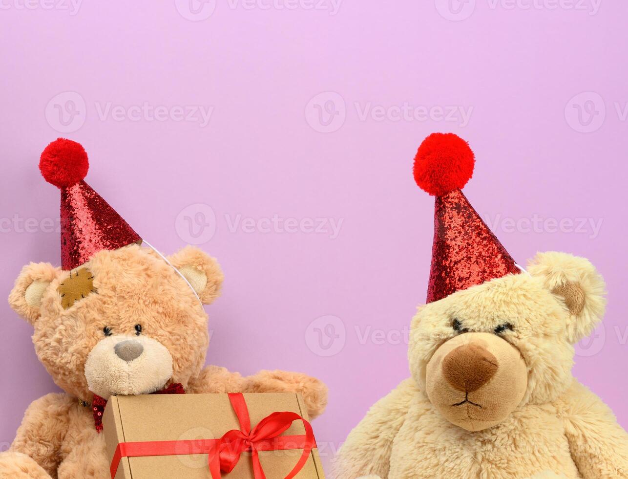 triste ours en peluche beige dans un bonnet rouge est assis sur un fond violet photo