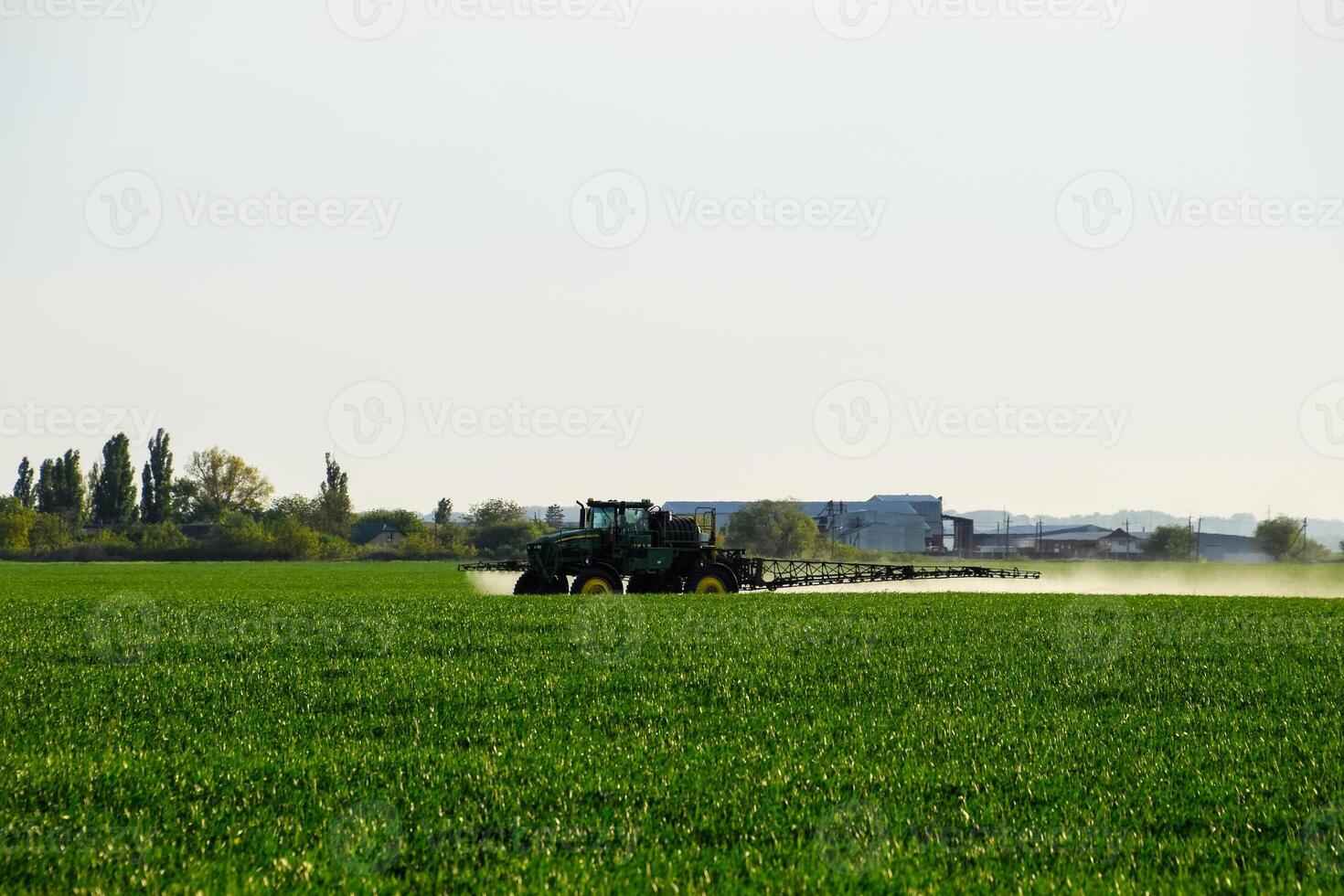 tracteur avec le Aidez-moi de une pulvérisateur Vaporisateurs liquide les engrais sur Jeune blé dans le champ. photo