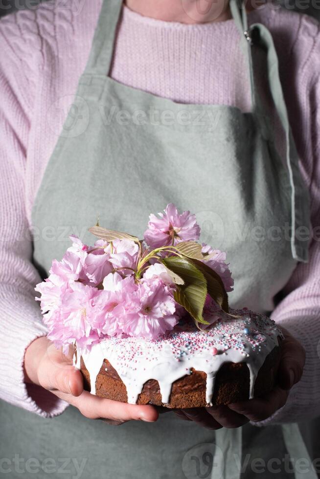 une femme décore une fait maison Pâques gâteau avec rose Sakura fleurs, printemps fleur photo