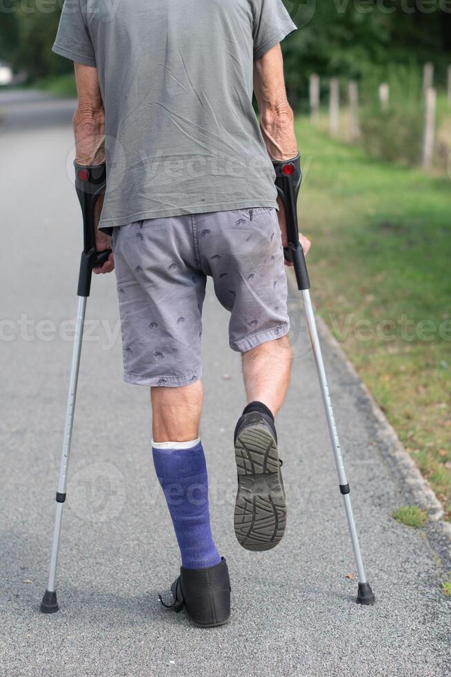 une homme avec une cassé jambe est en marchant vers le bas le rue, sur le sien la gauche jambe il a une spécial démarrage pour en marchant photo