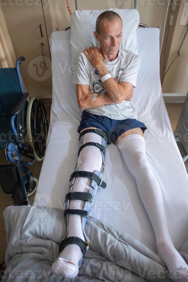 une homme avec une cassé jambe dans un orthèse sur une lit dans une clinique après un accident et une fracture de le fémur photo