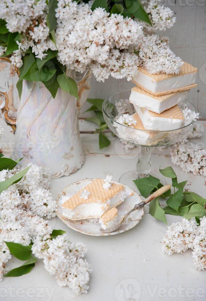printemps encore la vie avec une bouquet de blanc lilas, une empiler de gaufre la glace crème dans une bol et sur une soucoupe photo