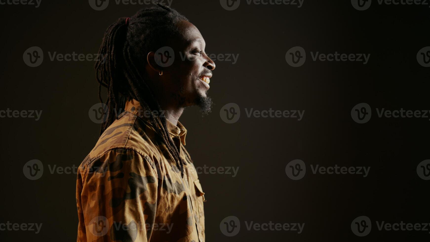 africain américain homme ayant amusement dans noir studio, en riant à blagues avec le sien copains et profiter bien ambiance sur caméra. Jeune la personne sentiment content et des rires à marrant mèmes. ordinateur de poche tir. photo