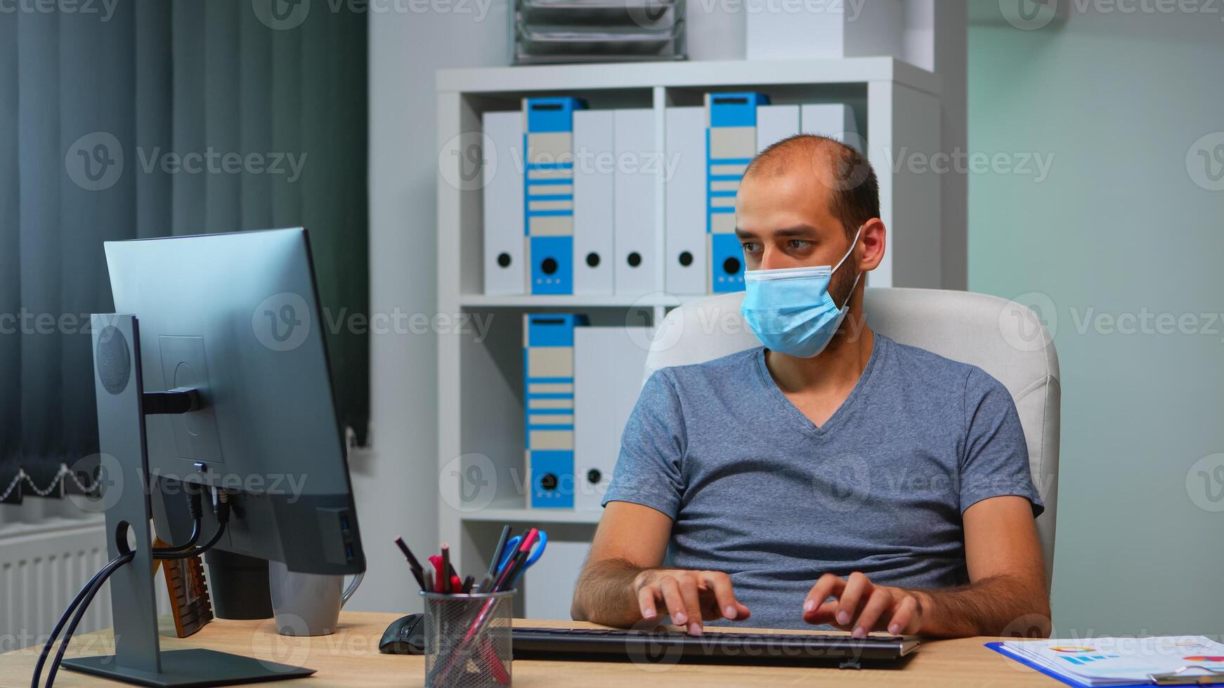 Jeune directeur avec protection visage masque travail seul dans Bureau pendant social distanciation. entrepreneur dans Nouveau Ordinaire personnel lieu de travail entreprise l'écriture sur ordinateur clavier à la recherche à bureau photo