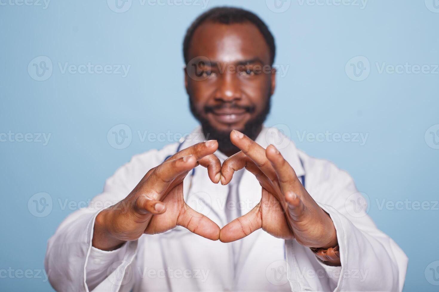 fermer de une cœur forme fabriqué par les doigts de un africain américain médical praticien. noir Masculin professionnel médecin habillé dans laboratoire manteau Faire l'amour main gestes vers le caméra. photo