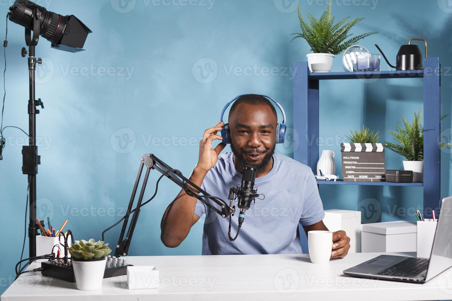 souriant l'Internet influenceur en buvant café et enregistrement vidéo avec écouteurs sur portrait. de bonne humeur blogueur parlant dans microphone avec les abonnés tandis que diffusion Podcast photo