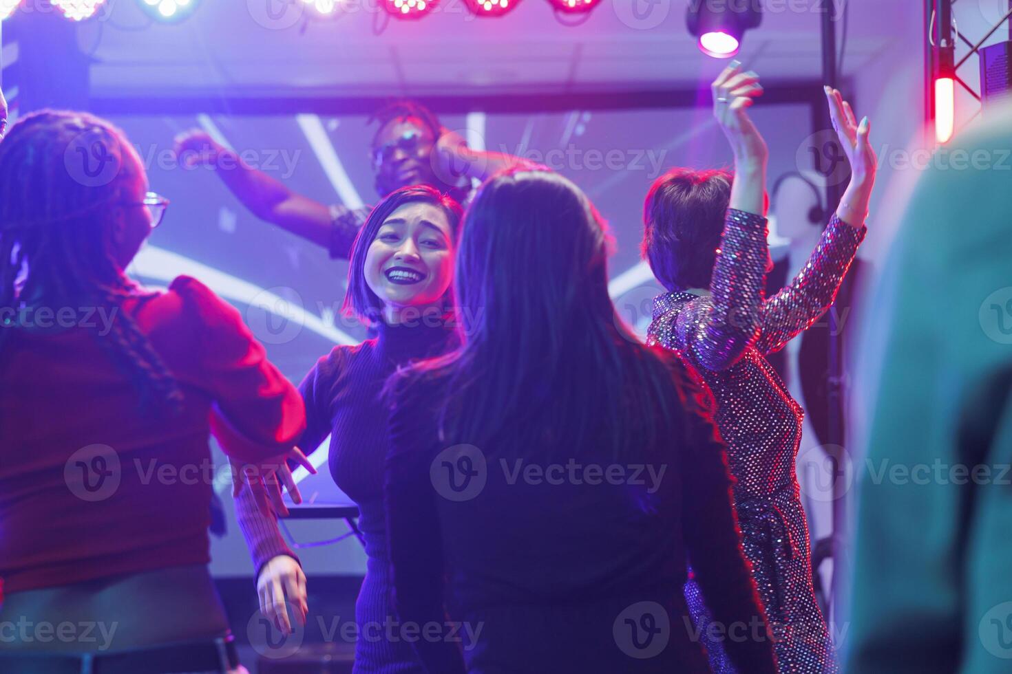 content diverse copines faire la fête et dansant à discothèque dans boîte de nuit. de bonne humeur souriant femmes en mouvement à la musique Beats, sauter et ayant amusement sur piste de dance dans club avec lumières photo