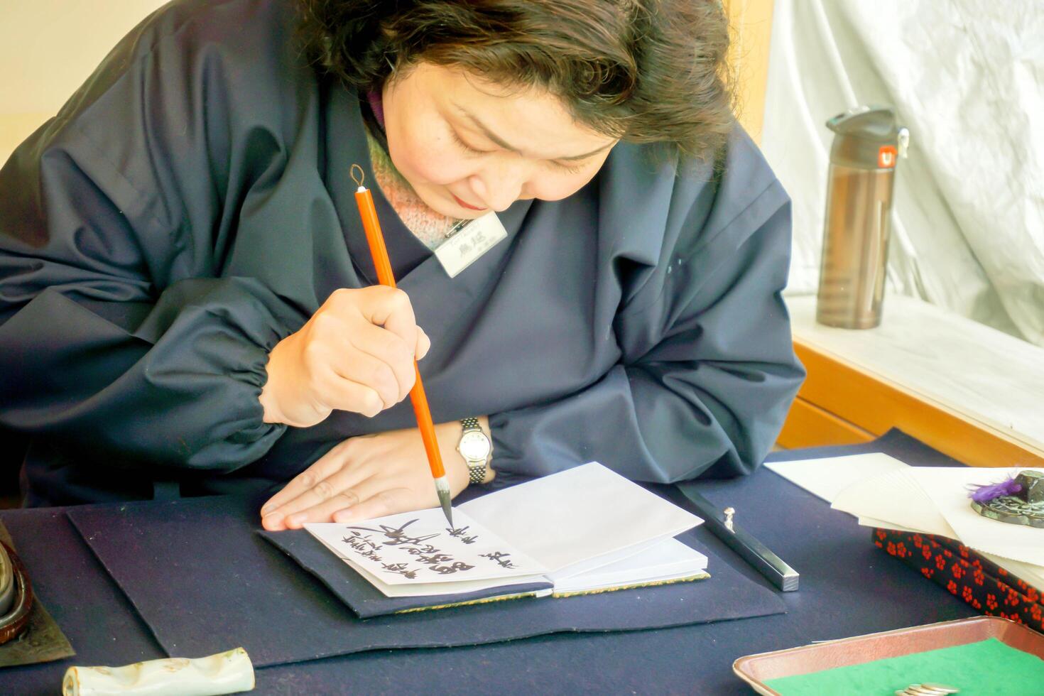 Kyoto ville, Japon, 2023 - Japonais femmes portant une bleu nationale robe et en portant une chinois brosse l'écriture Japonais des textes de noir encre sur une carnet papier. photo