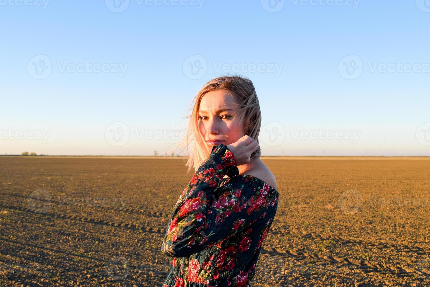 femme dans une labouré champ dans une rouge noir robe sur une le coucher du soleil Contexte. photo