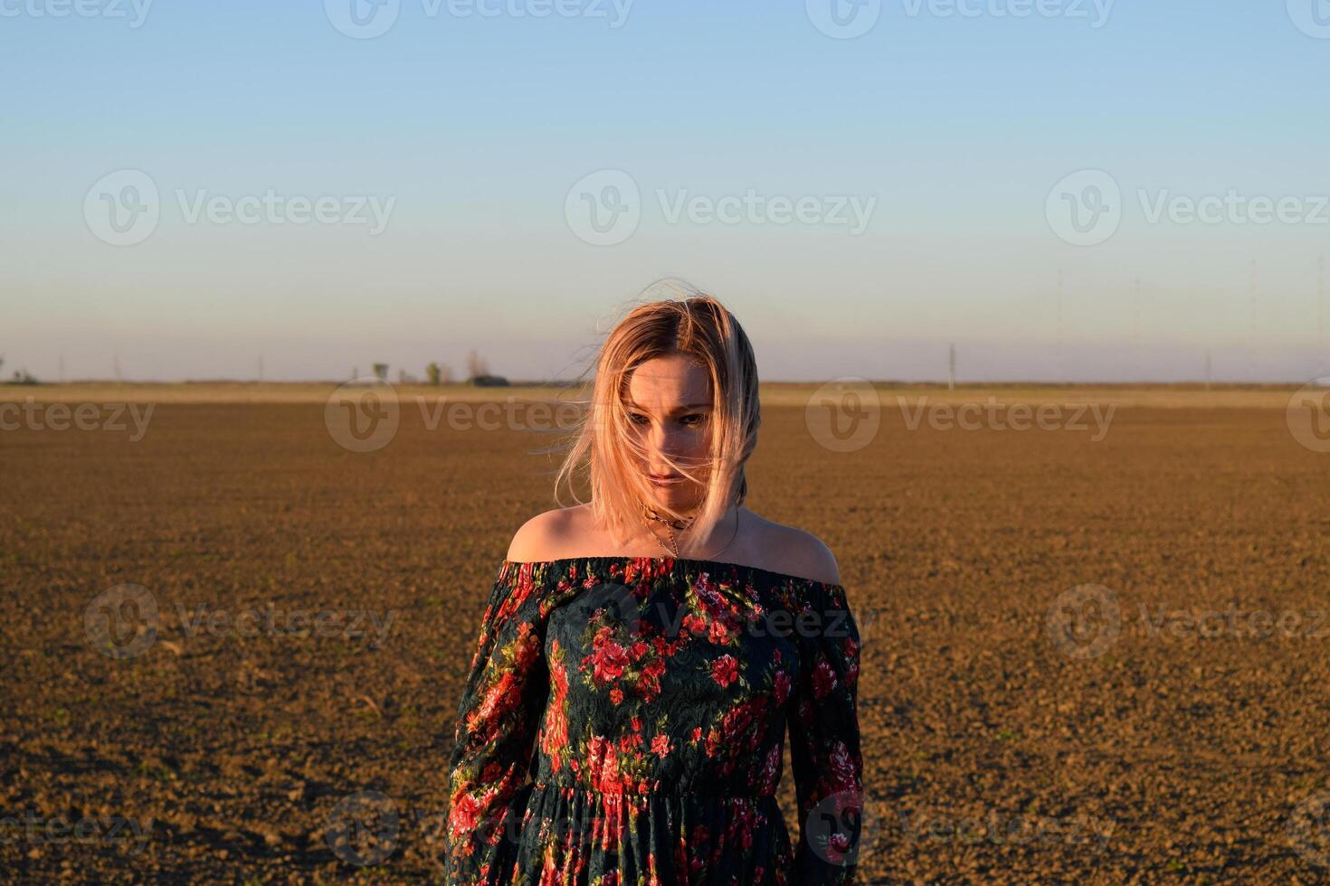 femme dans une labouré champ dans une rouge noir robe sur une le coucher du soleil Contexte. photo