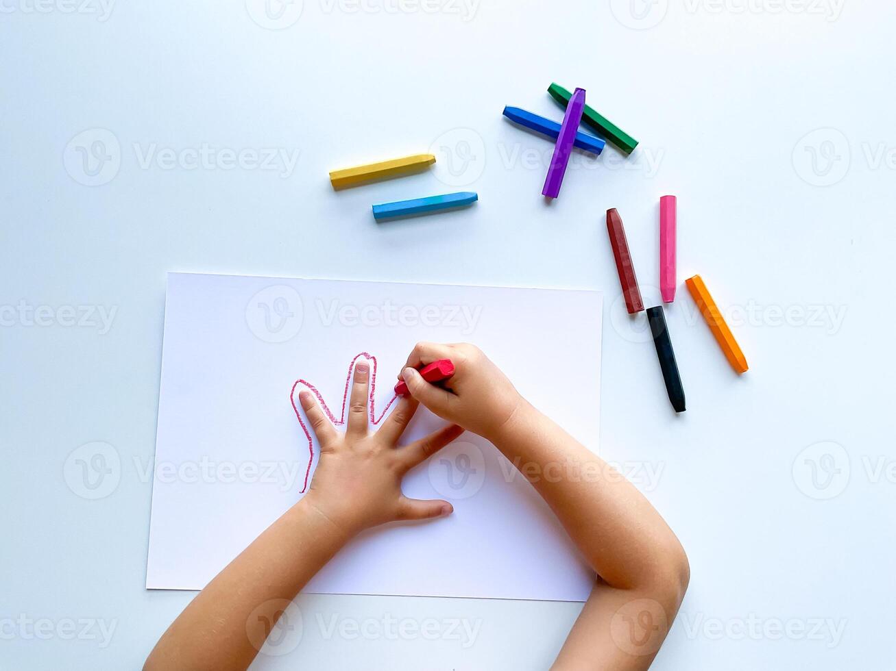 enfants mains dessiner leur main avec la cire crayons de couleur sur blanc papier, Haut voir. photo