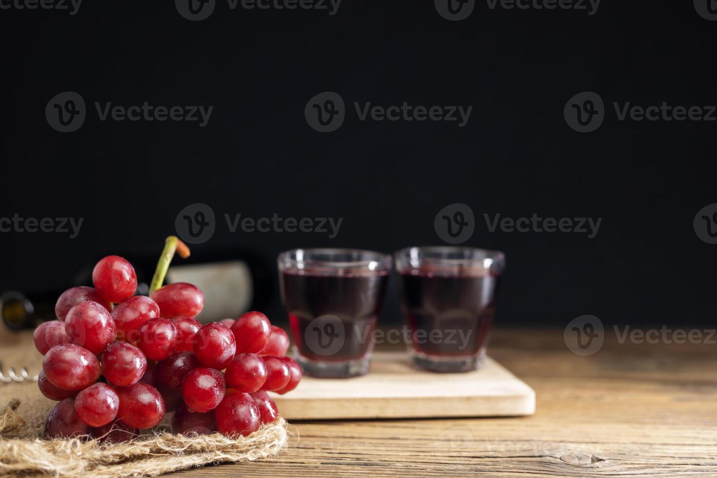 une bouquet de rouge les raisins avec rouge grain de raisin jus dans une verre mis sur une en bois table ou rouge vin, délicieux Naturel en bonne santé jus boire. photo