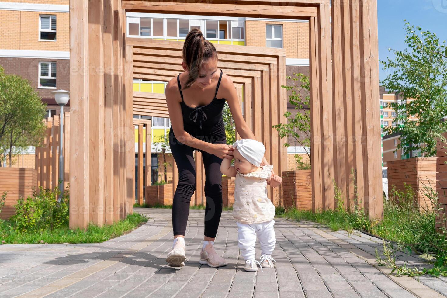 bambin bébé fille avec maman marcher dans le ville Cour, enfant apprend à marcher photo