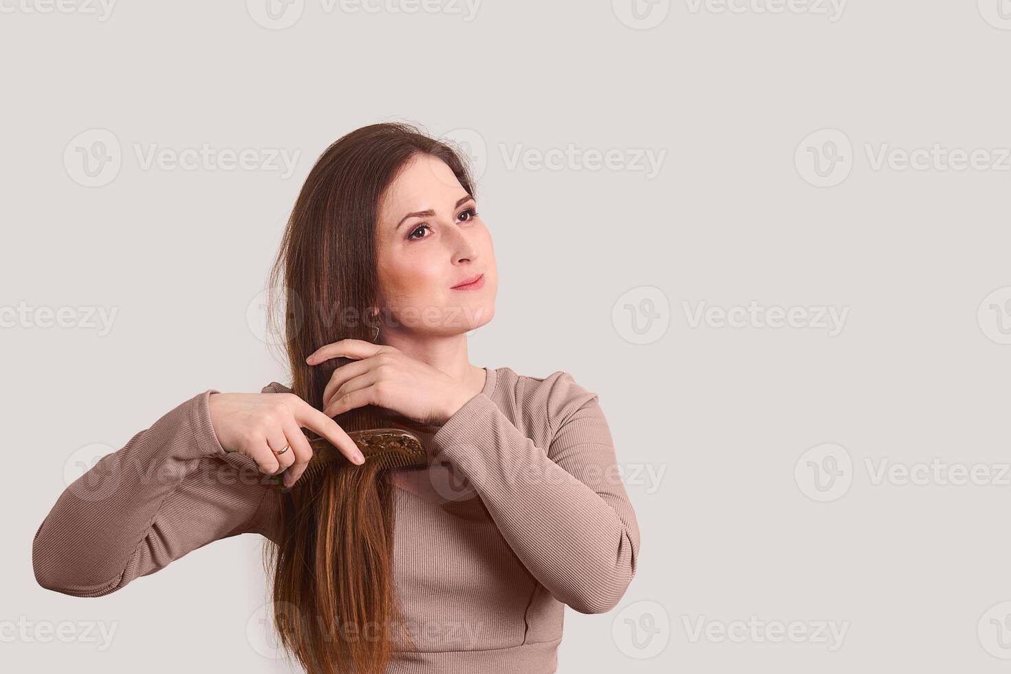 Jeune femme ratissage sa longue tout droit cheveux avec une peigne sur une lumière Contexte photo