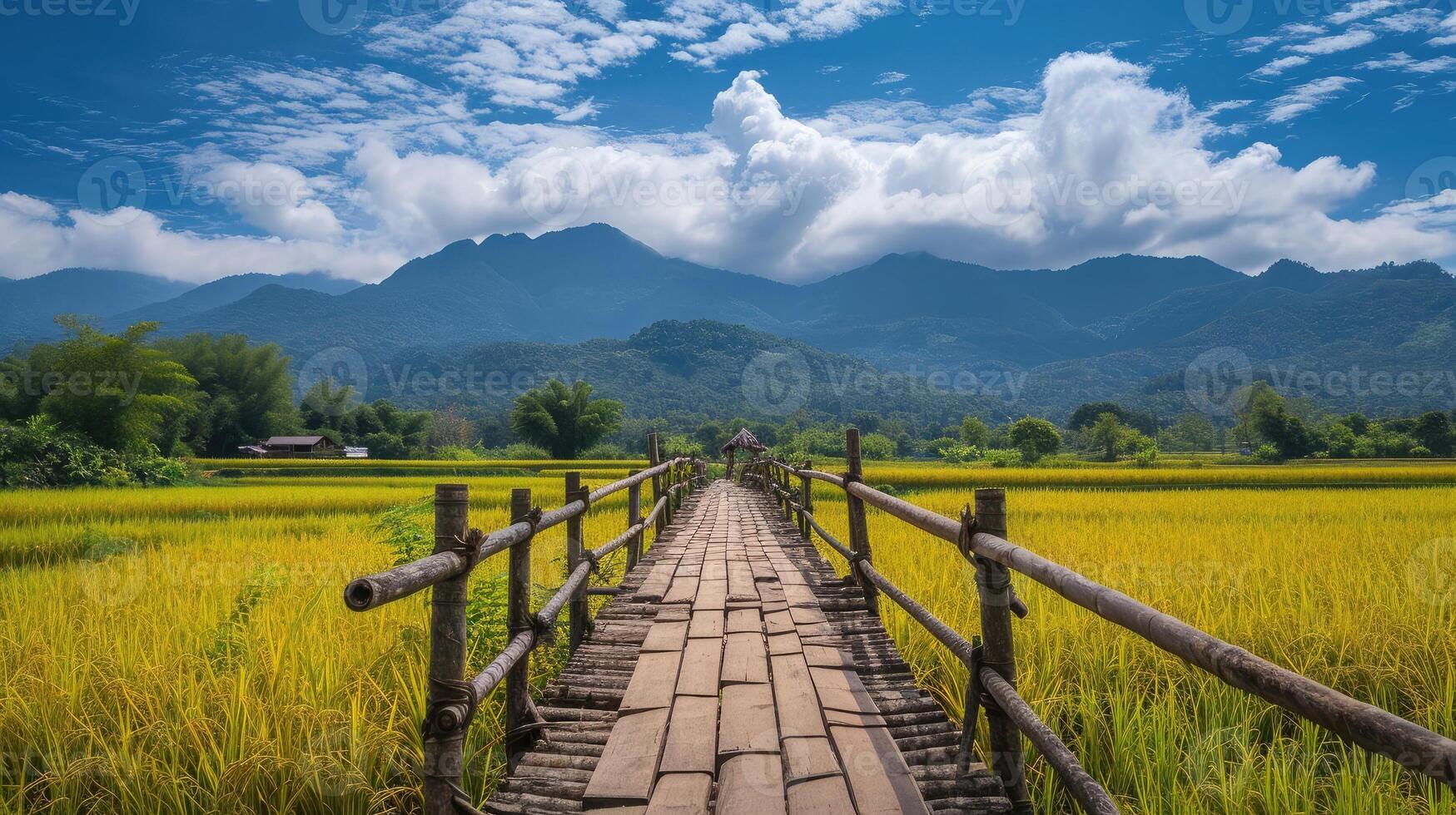 ai généré en bois pont s'étire à travers le Jaune riz des champs avec montagnes des nuages et bleu ciel dans Contexte photo