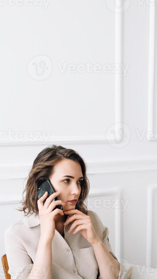 réfléchi millénaire femme engage dans une téléphone appel, pourparlers intensément, contemplativement assise sur une chaise, convoyer une sens de gravité et réfléchissant conversation photo