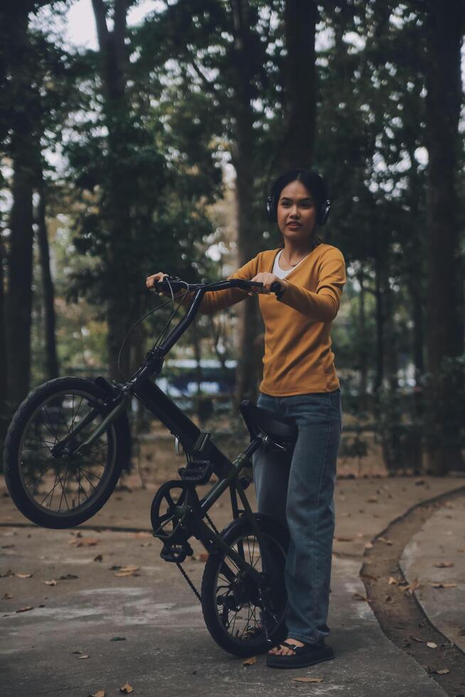 content Jeune asiatique femme tandis que équitation une vélo dans une ville parc. elle sourit en utilisant le vélo de transport. écologiquement amical concept. photo