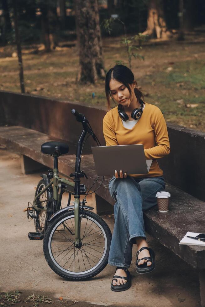 content Jeune asiatique femme tandis que équitation une vélo dans une ville parc. elle sourit en utilisant le vélo de transport. écologiquement amical concept. photo