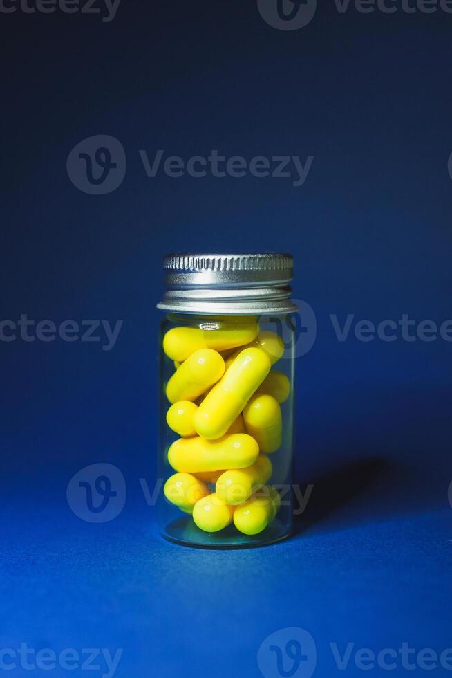 bouteille de clair verre avec Jaune pilules sur une bleu Contexte fermer verticale photo