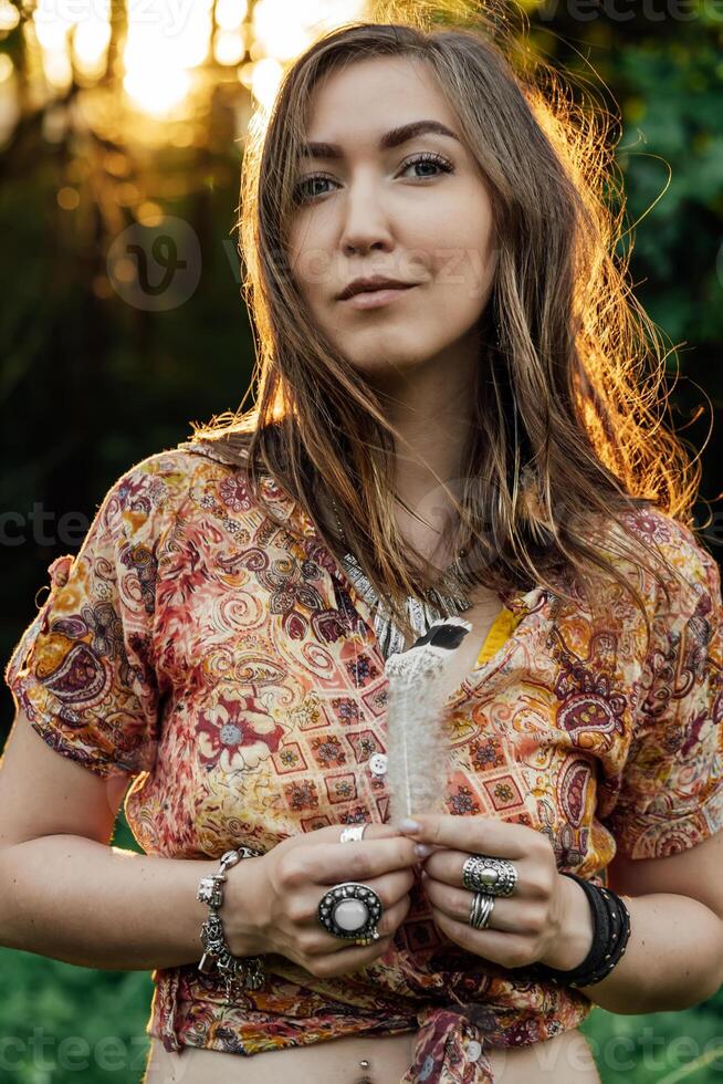 magnifique Jeune femme portant style bohème vêtements posant dans le des rayons de le soir soleil, le coucher du soleil. boho style mode, femelle portant argent bijoux ayant amusement dans parc en plein air. photo