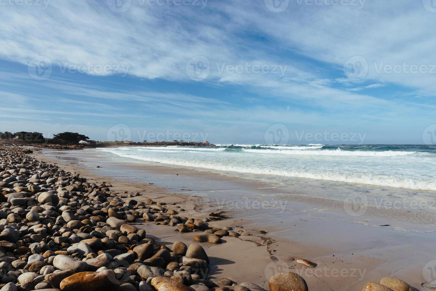 océan plage avec grand des pierres et le sable en dessous de une bleu ciel et des nuages photo