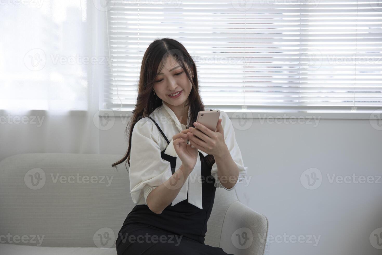 une Japonais femme vérification téléphone intelligent par éloigné travail dans le petit Bureau photo