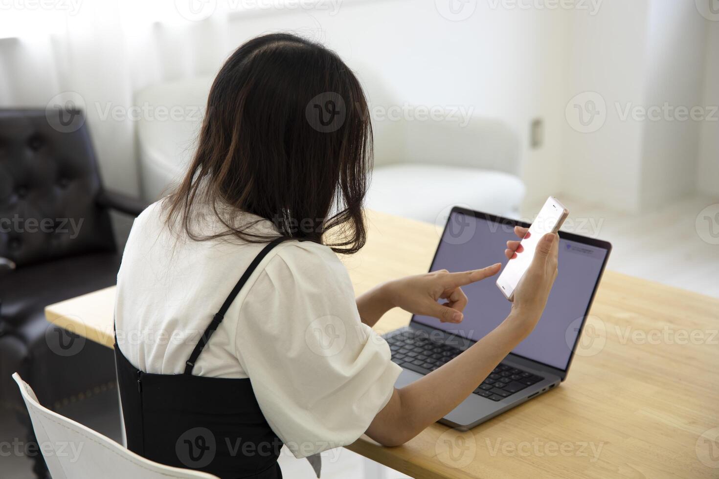 une Japonais femme vérification téléphone intelligent par éloigné travail dans le petit Bureau photo