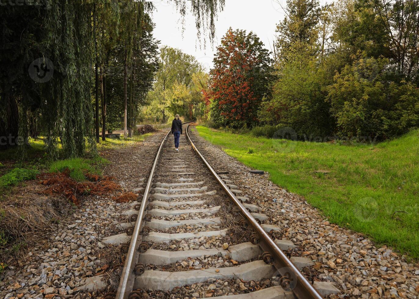 le fille des promenades le long de le chemin de fer Piste et là sont vert des arbres autour. sélectif concentrer photo