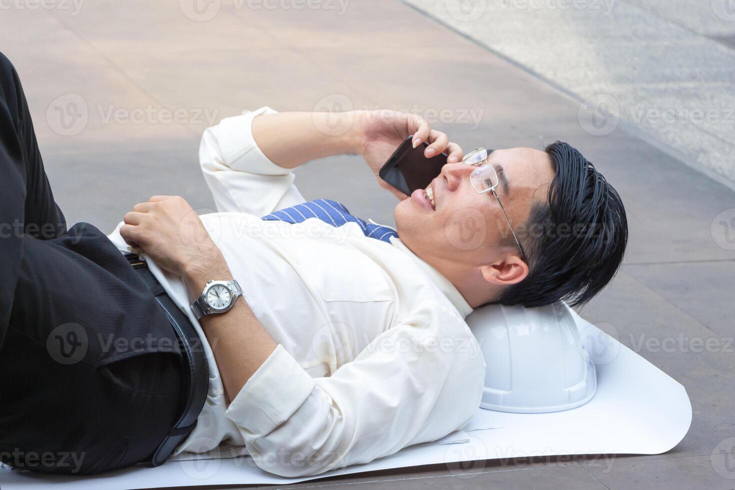 ingénieur homme relaxant et en utilisant téléphone intelligent sur le sol après travail difficile photo