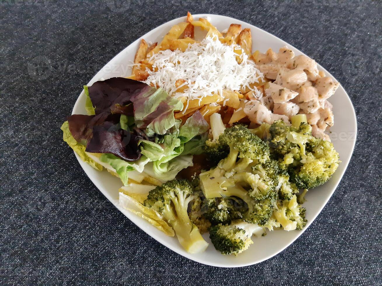 fait maison grillé poulet avec français frites, brocoli, fromage et vert salade, servi sur une blanc assiette photo