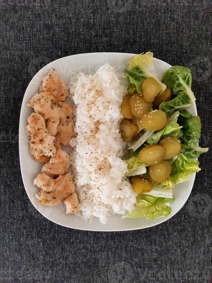 fait maison grillé poulet avec vert salade, riz pilaf et concombre cornichons servi sur une blanc assiette photo