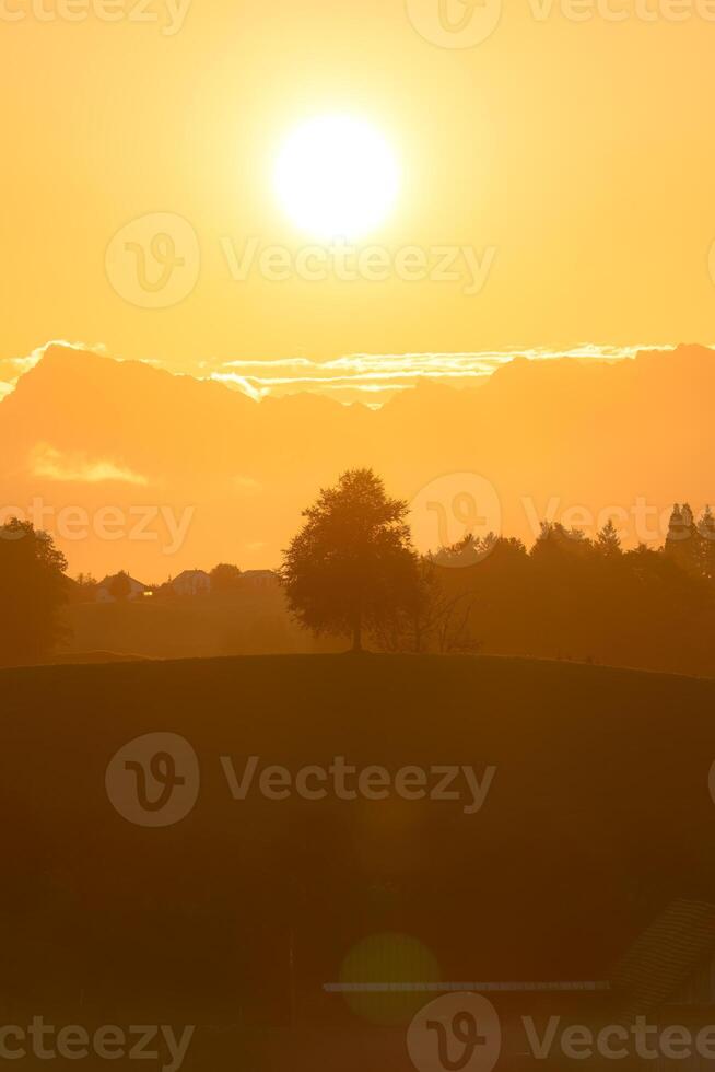 d'or lever du soleil plus de paisible village et arbre sur colline dans rural scène photo