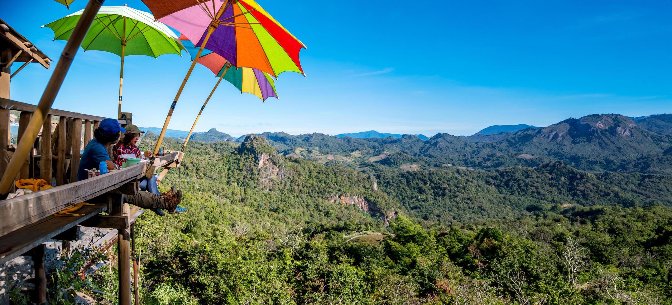 touristes asiatiques couple assis mangent des nouilles sur la plate-forme en bois et regardant une vue panoramique sur les belles montagnes naturelles à ban jabo, mae hong son, thialande. photo