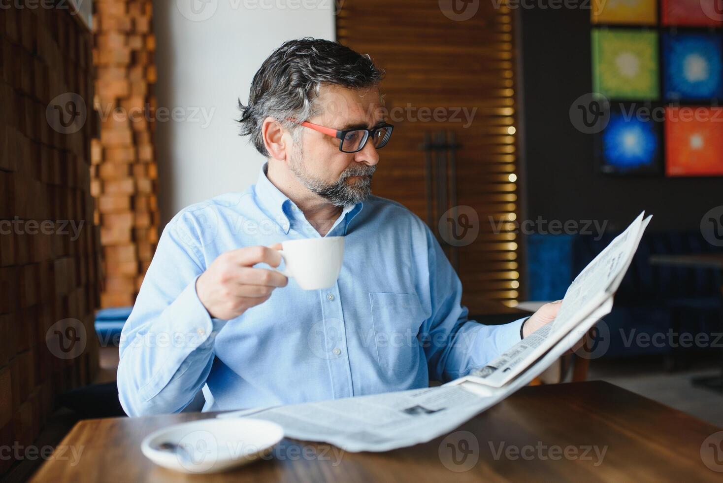 fermer portrait de sérieux Sénior Beau homme en train de lire journal, ayant café Pause et séance à tableau. photo