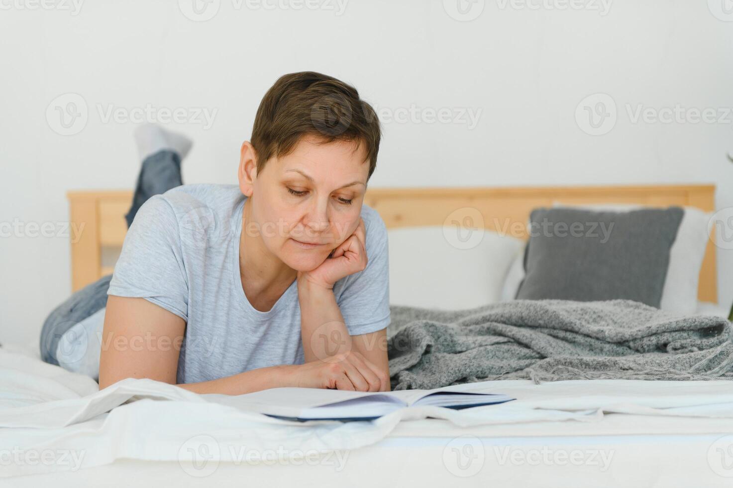plaisir et Accueil concept - souriant âge moyen femme en train de lire livre et mensonge sur canapé à maison. photo