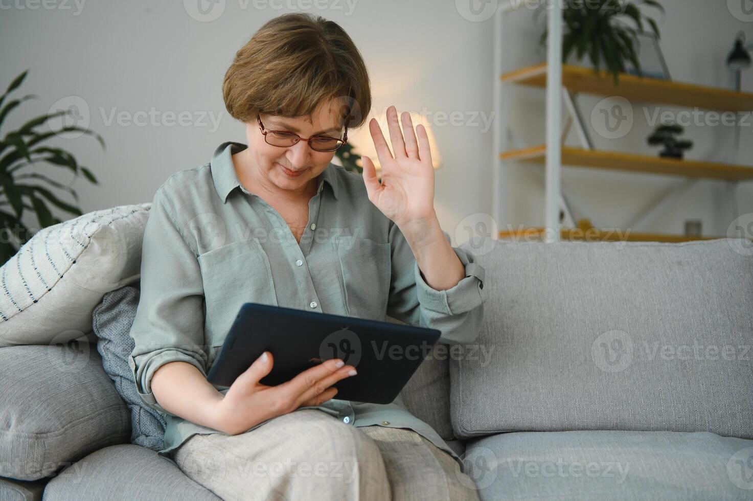 Sénior femme à la recherche et en riant à sa numérique tablette sur canapé photo