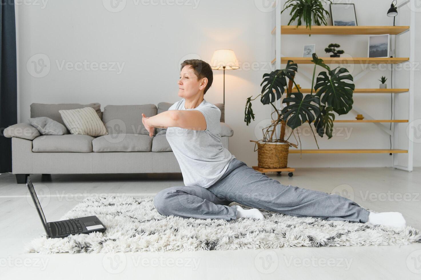 adulte femme Faire aptitude des exercices à maison. Sénior femme faire élongation des exercices. mature femme Faire yoga pose photo