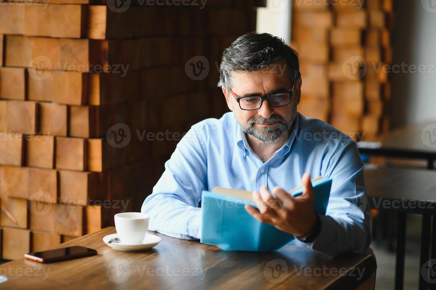 Sénior vieux homme en train de lire une livre dans une café boutique, profiter le sien littéraire loisir photo