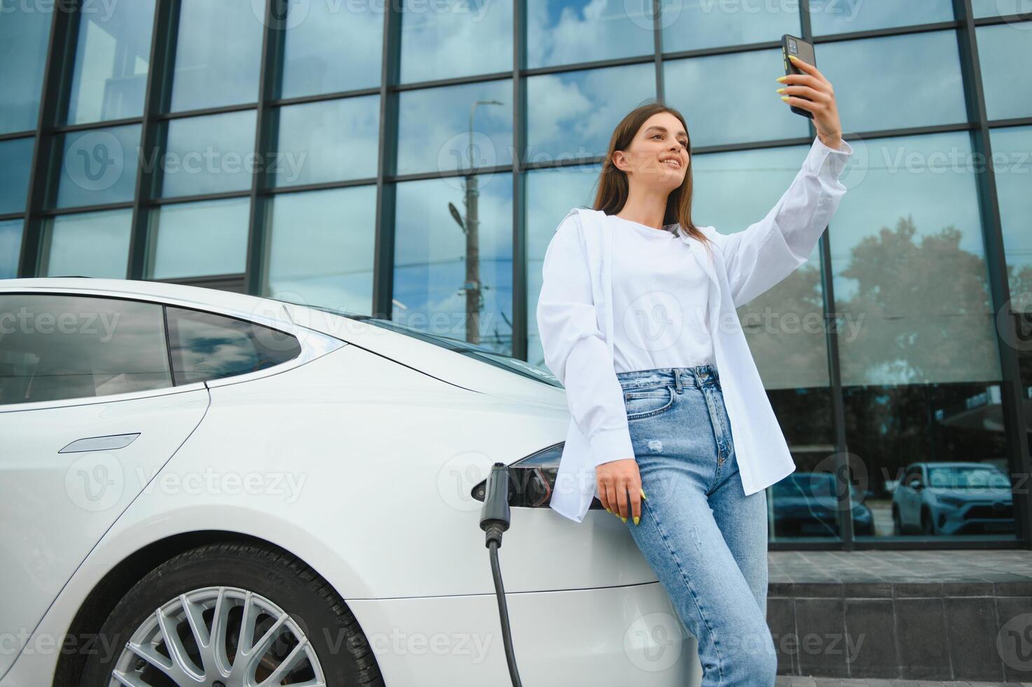 électrique voiture mise en charge dans rue. écologique voiture connecté et mise en charge batteries. fille attendre Puissance la fourniture relier à électrique Véhicules pour mise en charge. photo