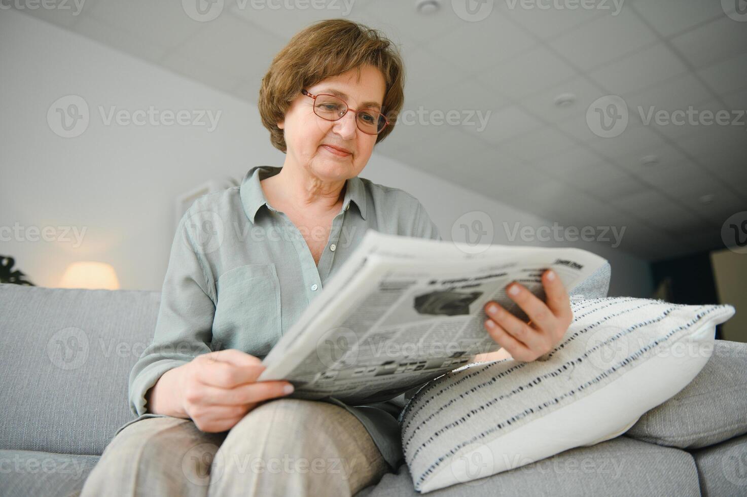 Sénior Dame en train de lire sa journal à Accueil relaxant sur une canapé et peering plus de le Haut à le téléspectateur photo