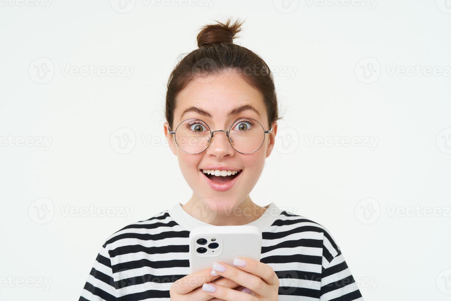 image de Jeune femme dans lunettes, en utilisant sa mobile téléphone, permanent avec téléphone intelligent et souriant, permanent plus de blanc Contexte photo
