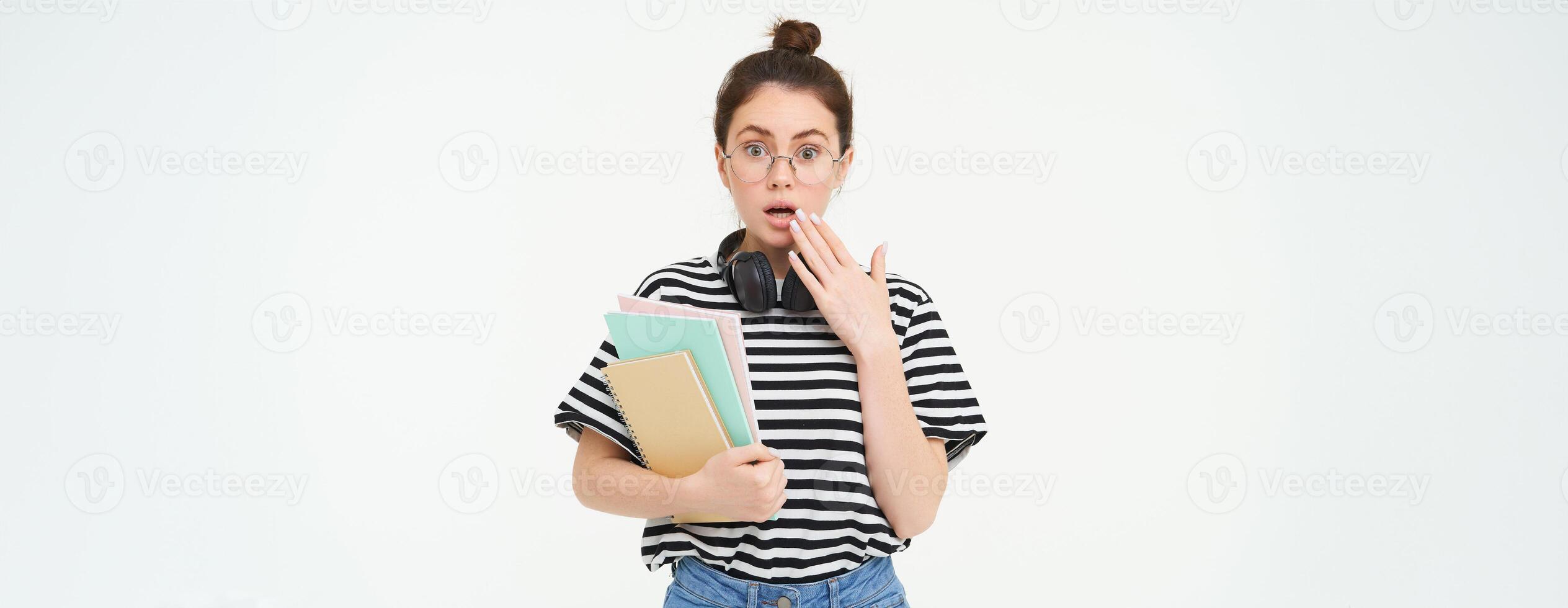 portrait de femme dans lunettes, étudiant regards surpris, halète et regards sous le choc à caméra, détient des cahiers et étude matériel, blanc Contexte photo