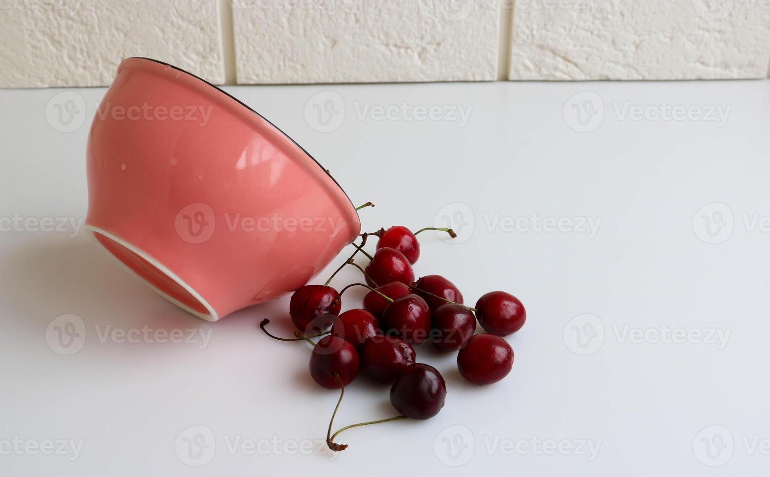 une Cerise avec gouttes de l'eau mensonges sur le blanc cuisine table suivant à une rose bol. rustique fruit Contexte. photo