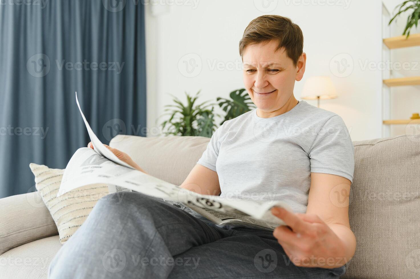 milieu vieilli femme séance canapé et en train de lire journaux. photo